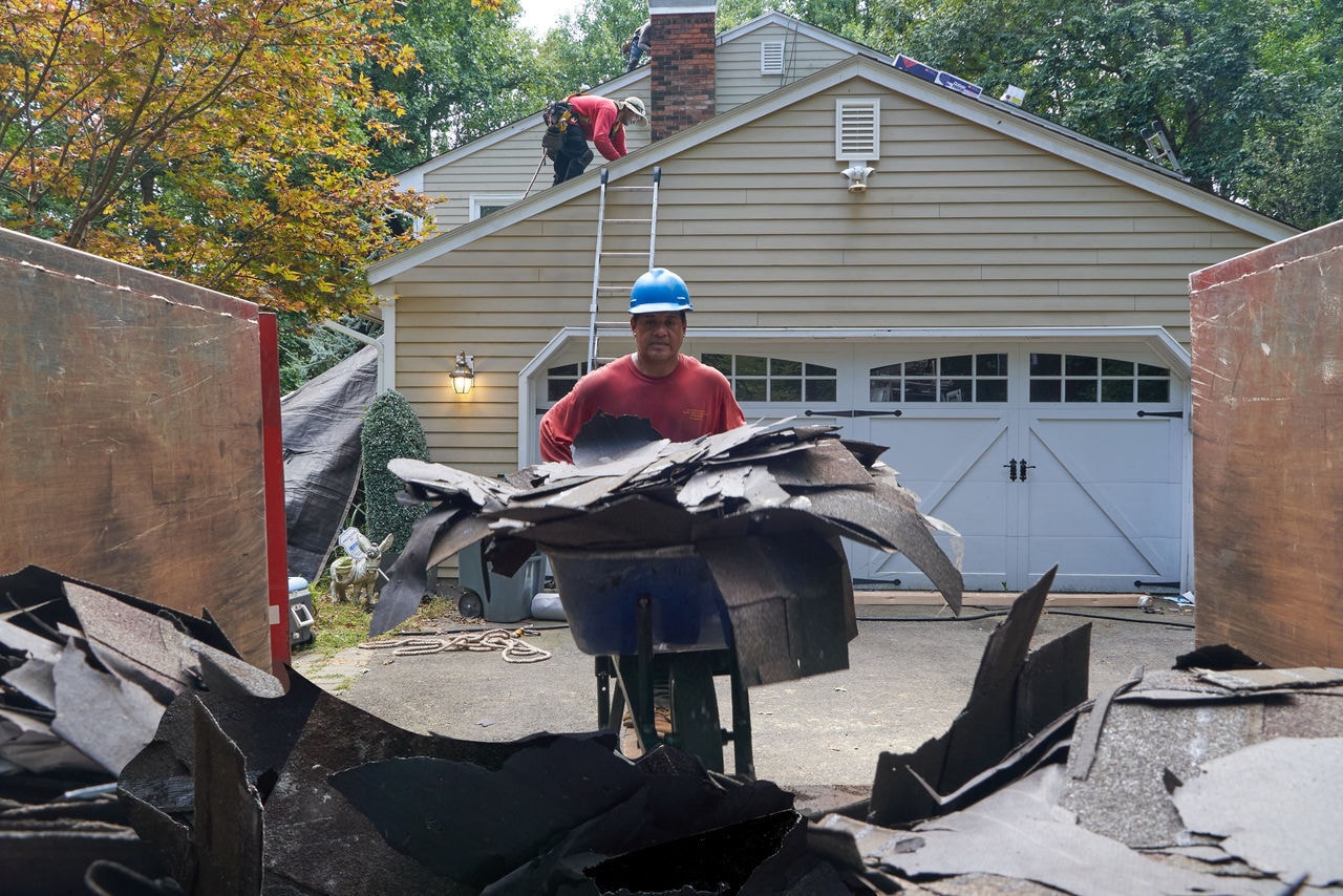 A roofer hauling roofing debris to a dumpster