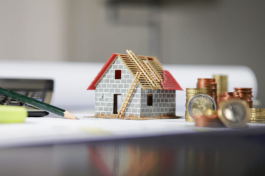Toy house with a roof being repaired, alongside a calculator and a stack of coins