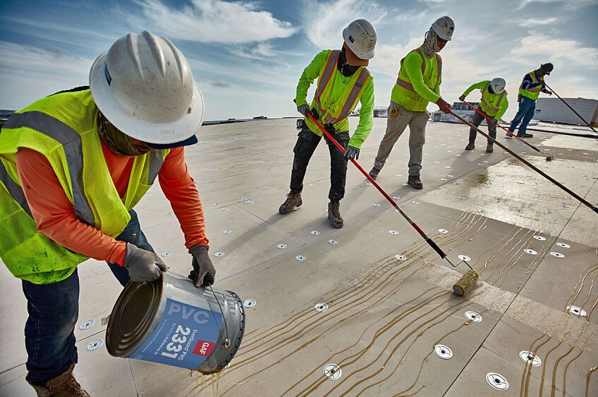 A group of five roofers installing GAF PVC products on a commercial roof