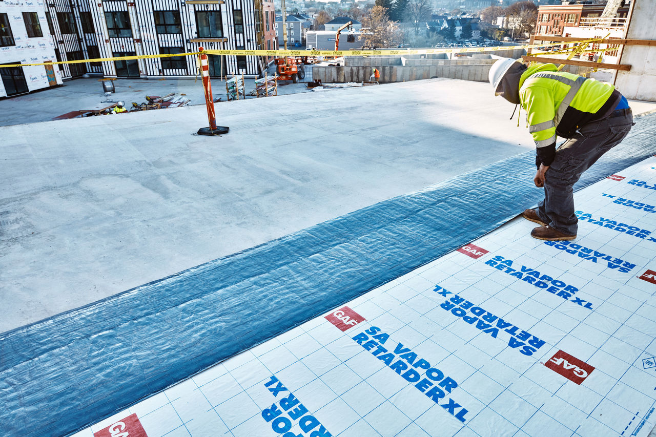 A roofer installing GAF SA Vapor Retarder XL on a roof