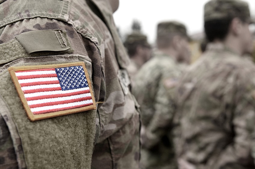 Shadow of a soldier saluting in front of a backlit American flag.
