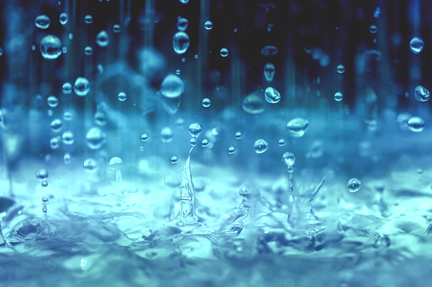 A close-up, blue-tinged image of raindrops falling into water.