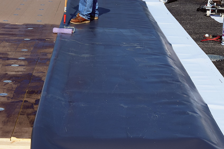 A contractor applying GAF EverGuard® adhesive with a roller