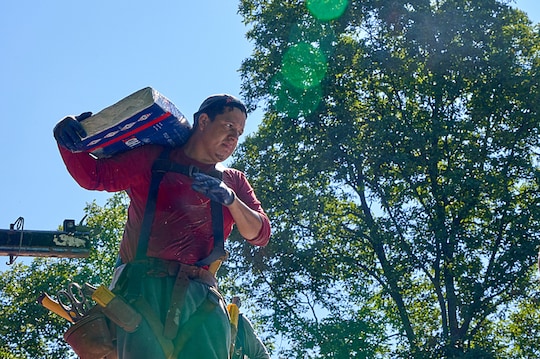 A roofer carrying a bundle of shingles on top of a residential roof