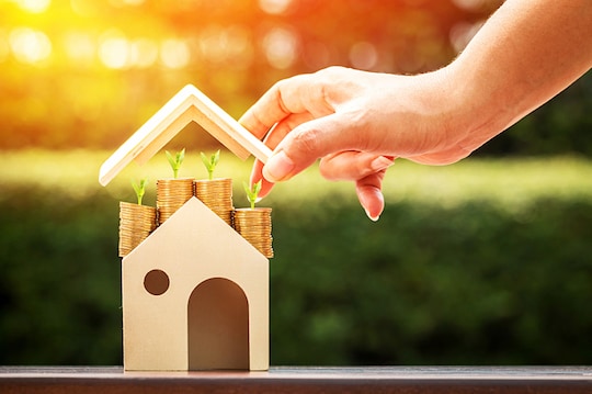 Hand placing a roof above a wooden home