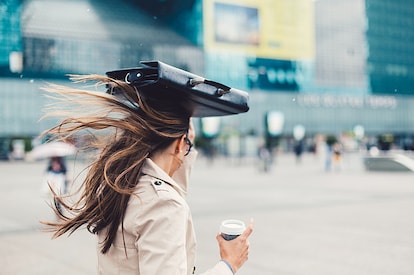 woman in rain with brief case over head by office building