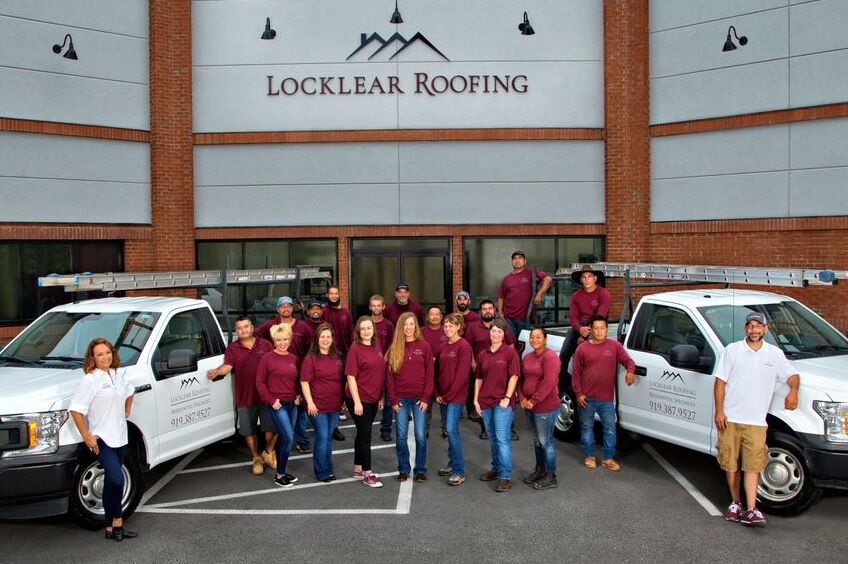 The Locklear Roofing team in front of their headquarters posing near a pair of work trucks.