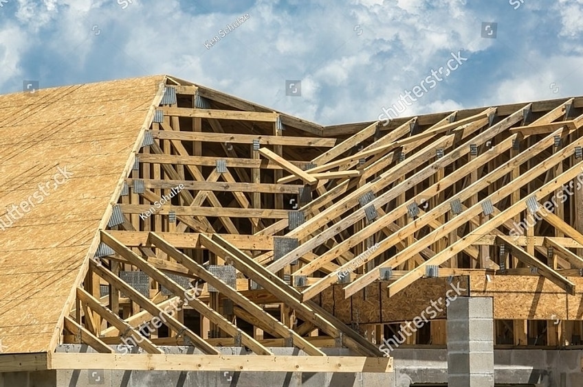 A roofer wearing a reflective yellow vest installs plywood roof decking