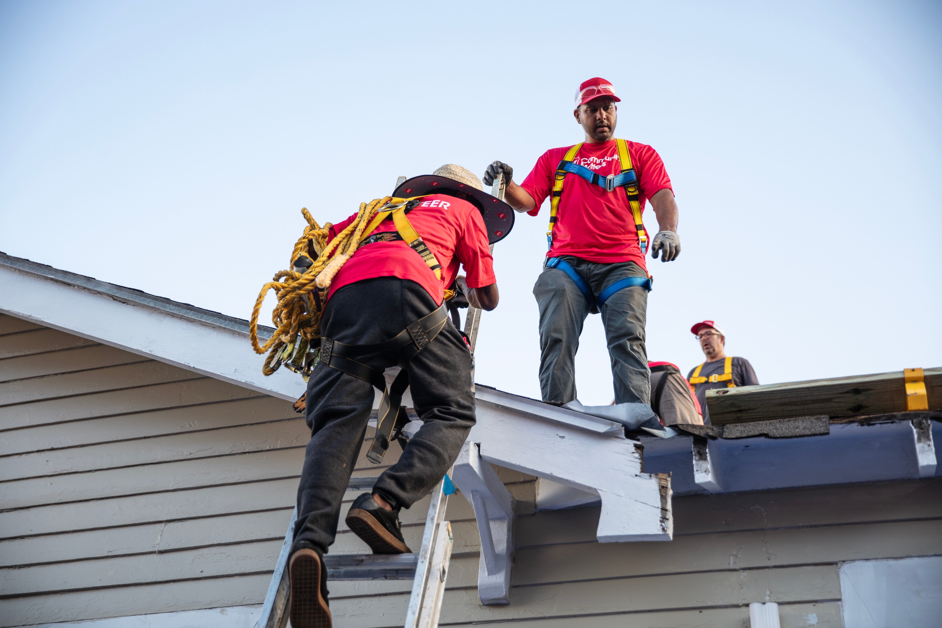 Gary Pierson stands on a roof while a volunteer climbs a ladder