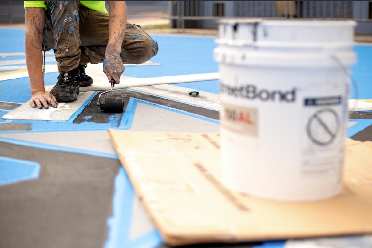 Installer is seen painting custom StreetBond colors on the sports court in Orlando