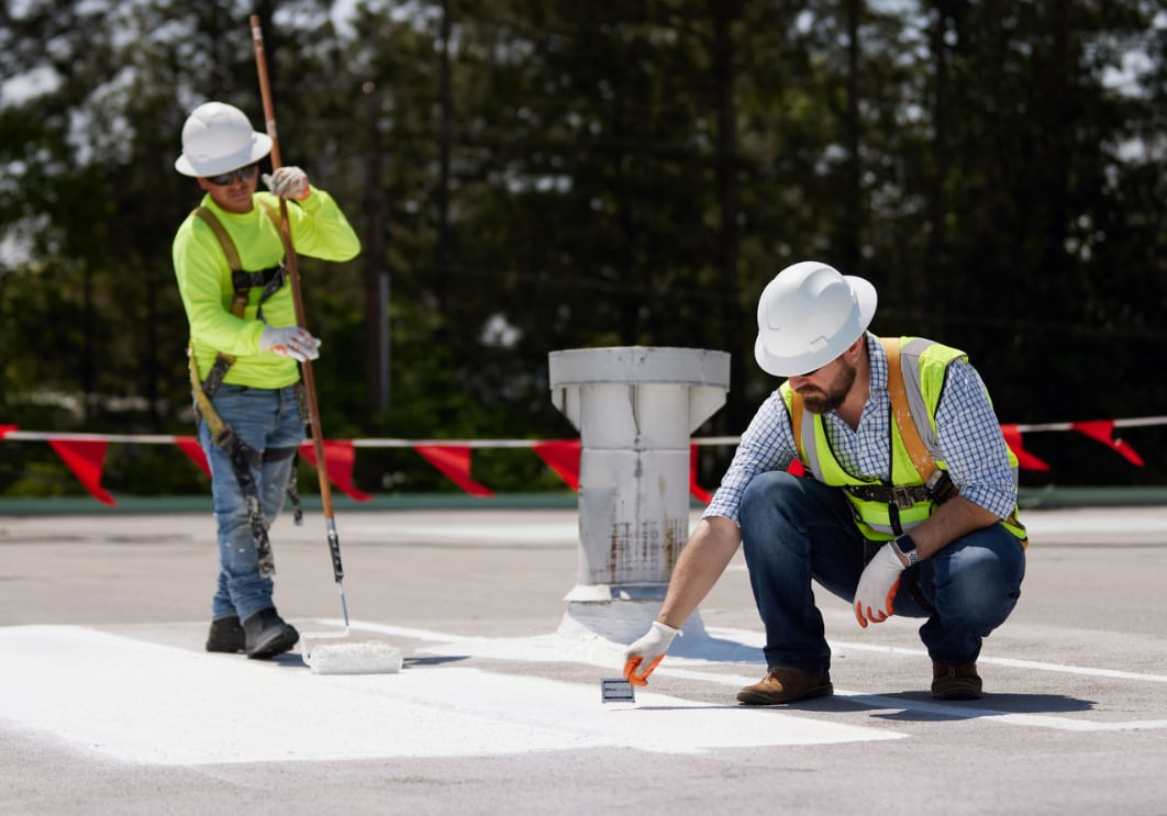 Two roofers installing a silicone roof coating on a commercial building.