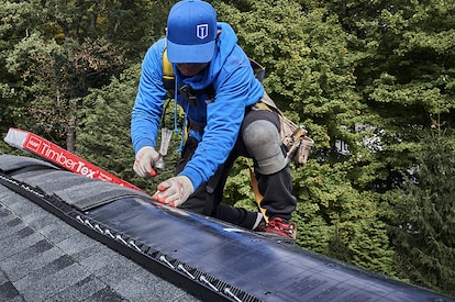 Roofer installing GAF TimberTex ridge cap shingles on the roof of a house.