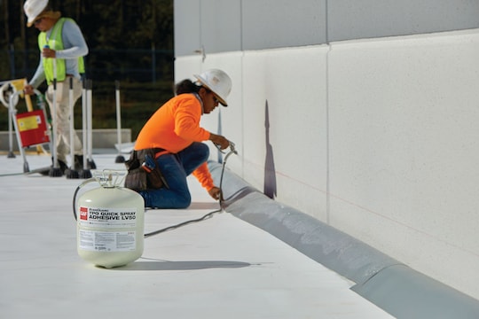 A roofer installs GAF's TPO Quick Spray Adhesive on a flat roof