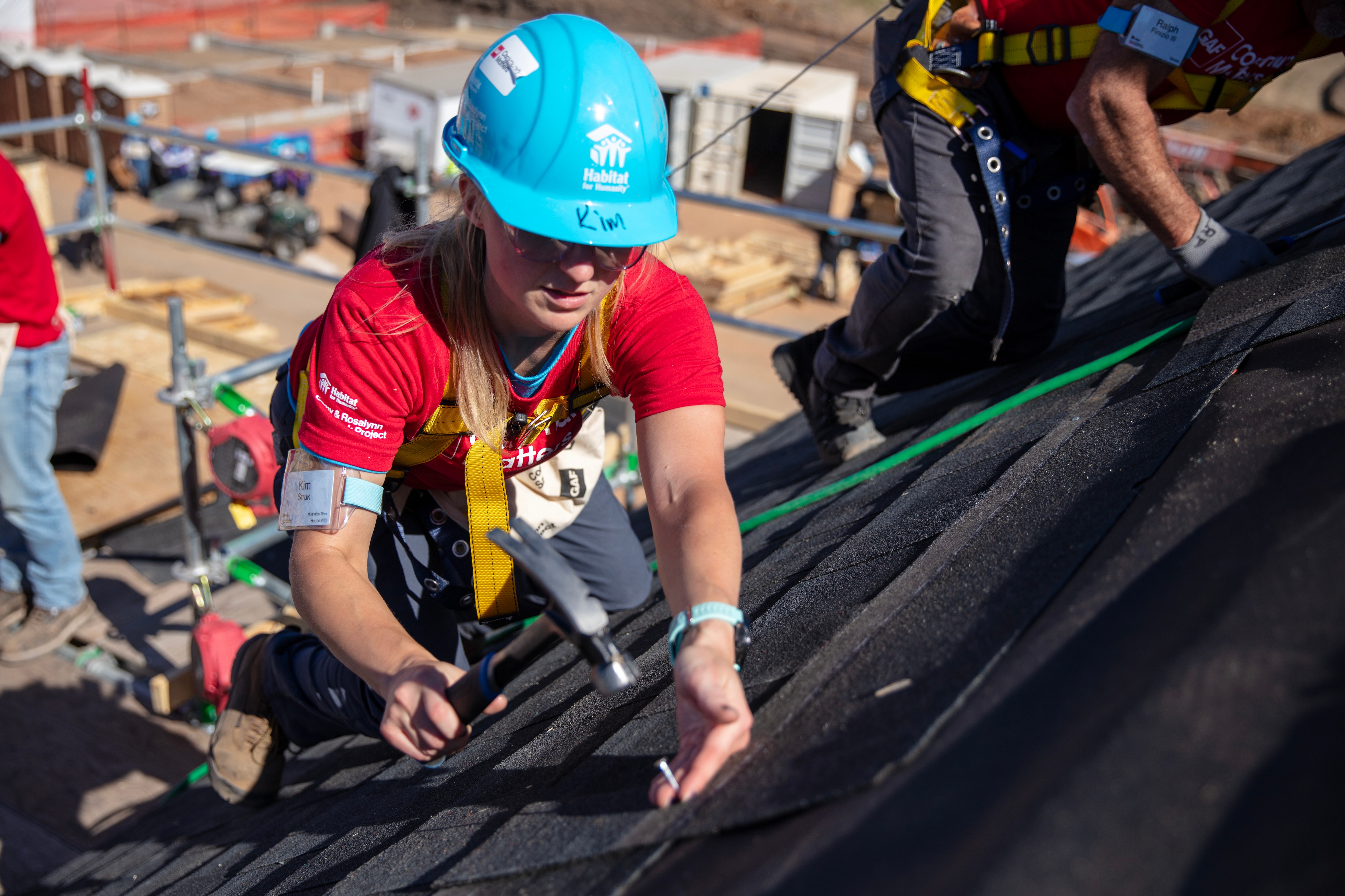 White woman in red shirt installing GAF shingles.