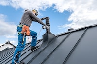 A roofing contractor installs a chimney cricket using a drill.