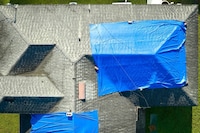 A damaged residential roof is covered by two blue tarps.