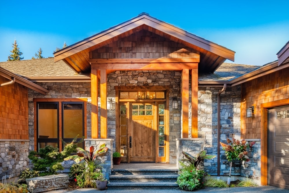 Front entry doorway with cedar beams stone trim and pillars bright blue sky and dappled shadows Front entry doorway with cedar beams stone trim and pillars bright blue sky and dappled shadows