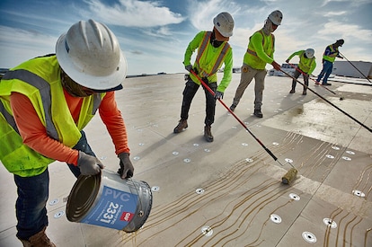 A group of five roofers installing GAF PVC products on a commercial roof