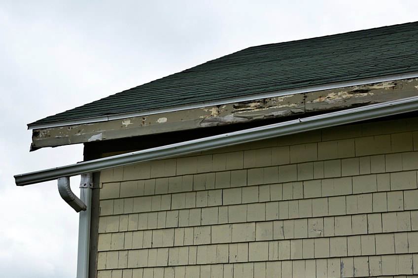 A broken gutter hanging off roof due to storm damage.