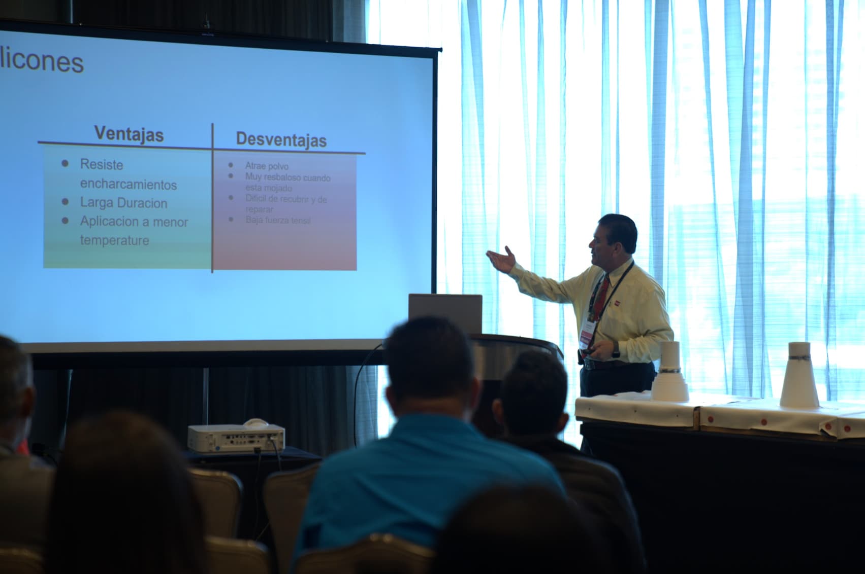 latinos in roofing 2023 spanish presentation A man stands at the head of a room to give a roofing presentation to a class in spenish.