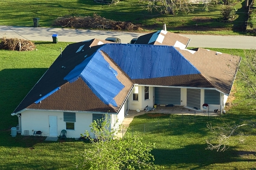 Hurricane Ian damaged house rooftop covered with protective plastic tarp against rain water leaking