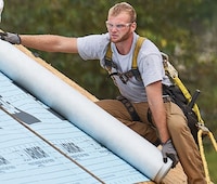 Professional roofer safely installs deck armor on the roof of a home