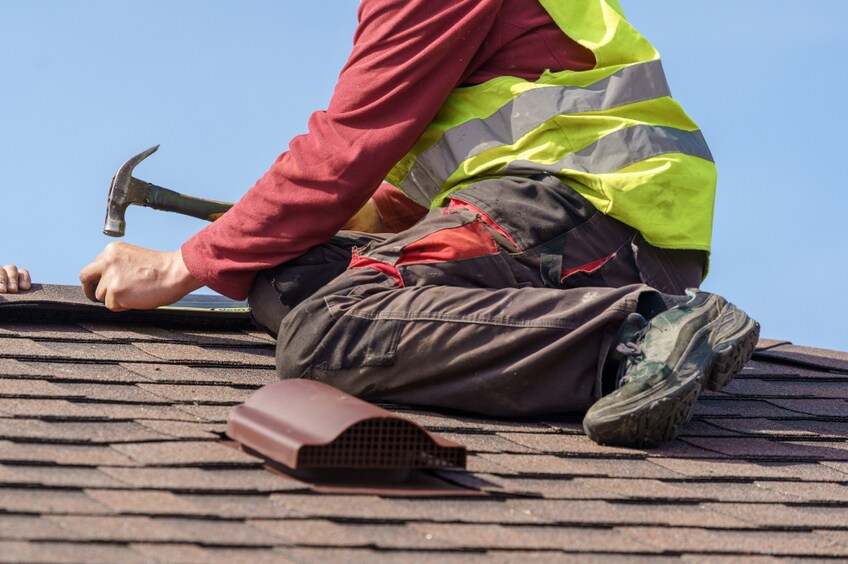 Concept of construction process. Two skilled roofer in special work wear with helmet in hands installing asphalt shingle or roof tile on top of new house