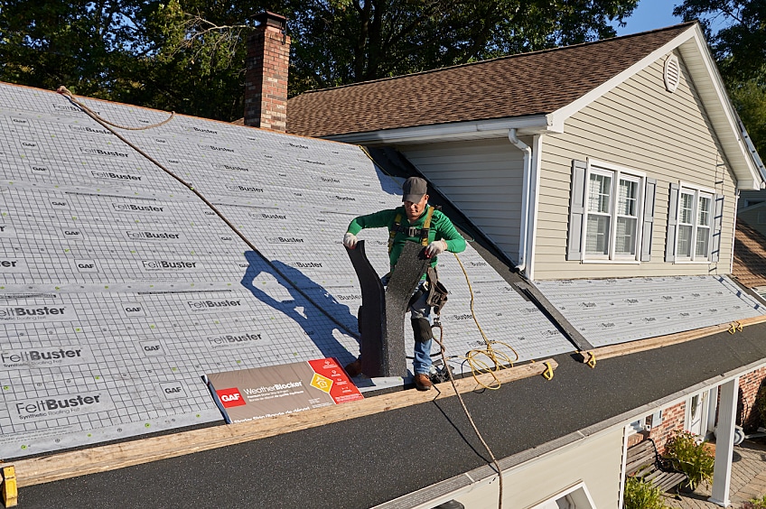 Roofing contractor on top of roof splitting a shingle starter strip for proper installation