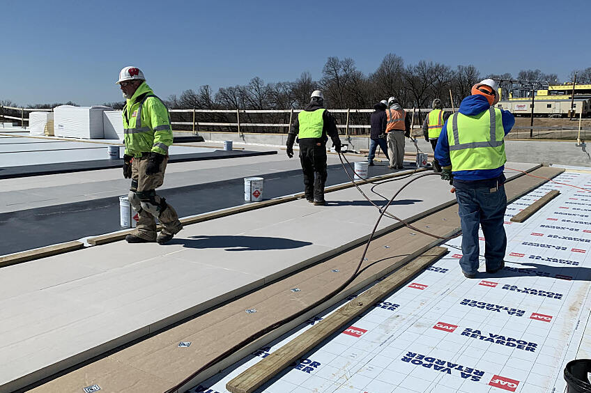 Construction workers install vapor retarders on a commercial roof
