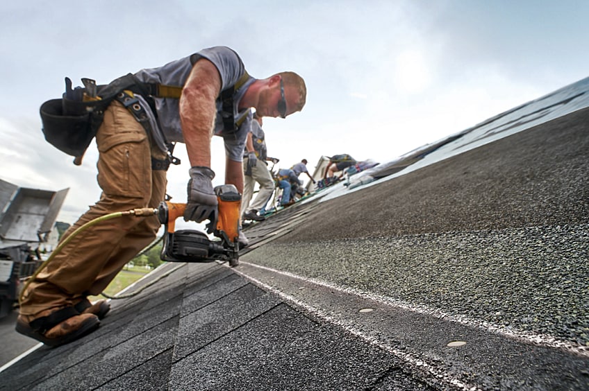A man with ha nail gun installs shingles